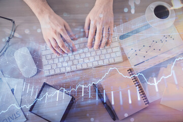 Multi exposure of man's hands typing over computer keyboard and forex graph hologram drawing. Top view. Financial markets concept.