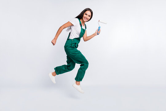 Photo of crazy pretty lady jump go hold roller look camera wear green overall shoes isolated white color background