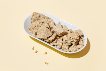 Sunflower seed halva in a white plate on a yellow background. Traditional oriental sweets. Jewish, Turkish, Arabic national dessert. Turkish sweets concept