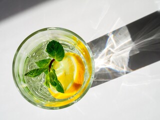 Top view of the glass of water, lemon and mint. Wellness, healthy food, drink, diet, detox. Fresh summer lemonade. Shadows on white background. Sun lighting. Copy space