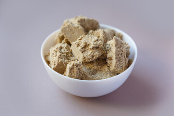Halva slices in a white cup on a colored background, close-up