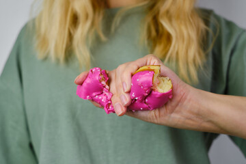 Crushed pink doughnut in the hands of a girl. Delicious sweet american dessert. Popular baked goods. Donut in bright sugar glaze close-up. Woman posing with donut in her hands. Fast food