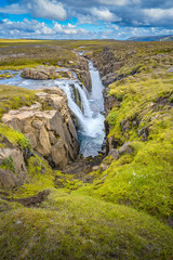 Naklejka na ściany i meble Lonely canyon waterfall in Highlands of East Iceland at summer sunny day and blue cloudy sky.