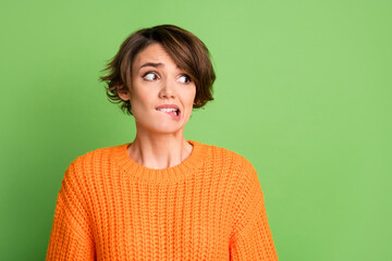 Portrait of stressed nice brunette lady bite lip look empty space wear orange sweater isolated on pastel green background