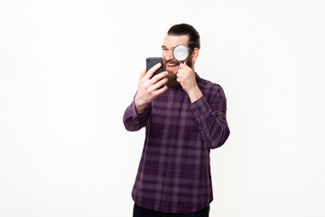 Photo of handsome man in checkered shirt looking trough magnifying glass at smartphone