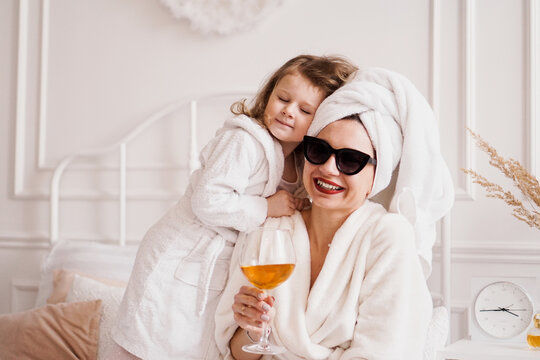 Mother And Daughter In The Bedroom In Bathrobes. The Girl Hugs Her Mom