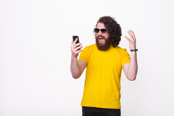 Photo of young hipster man with beard and long curly hair screaming at smartphone