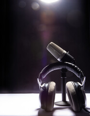 professional condenser microphone and headset on white surface and black background, low key portrait, selective focus.
