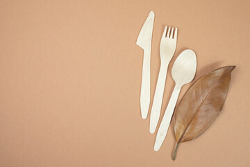 Disposable bamboo cutlery and dry natural magnolia leaf on a beige background.