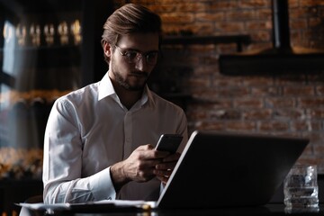 Casual man relaxed using smart phone, young man browsing on smart phone in cafe interior.