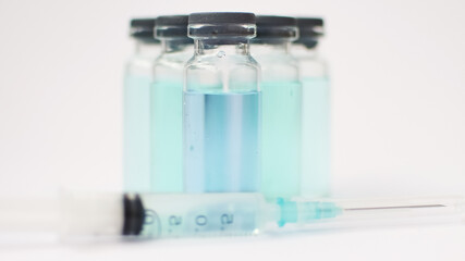 Vial vaccine, glass ampoules with transparent and blue liquid, a syringe is lying near on white background, global vaccination concept