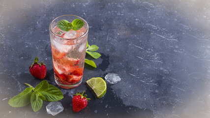 Mojito cocktail with ice cubes. Glass of Summer lemonade or ice tea. Refreshing cool detox drink with strawberry, lime and mint on dark background. Healthy eating. Сopy space for text.