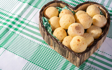 Cheese bread, heart-shaped basket lined with green and white fabric filled with cheese bread on a checkered tablecloth, selective focus.