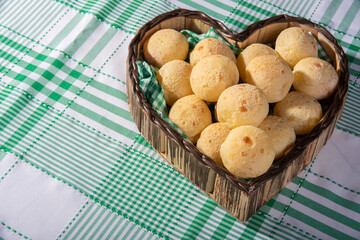 Cheese bread, heart-shaped basket lined with green and white fabric filled with cheese bread on a checkered tablecloth, selective focus.