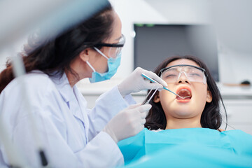 Dentist using dental mirror and tweezers when checking teeth of young female patient