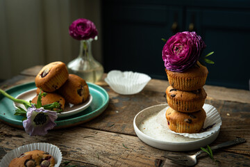 Homemade cherry and chocolate muffins and ranunculus and anemone flowers on rustic wooden table. 