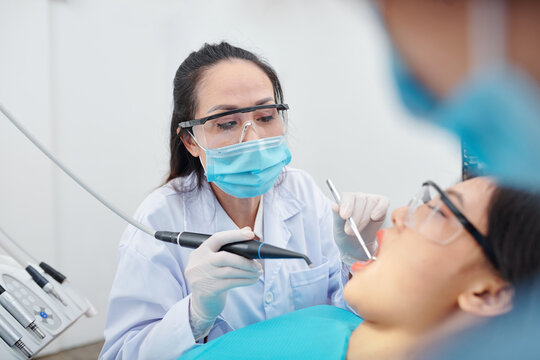 Mature experienced dentist in goggles and protective mask drilling teeth of patient suffering from cavity