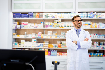 Portrait of smiling caucasian pharmacist standing in drug store with arms crossed.