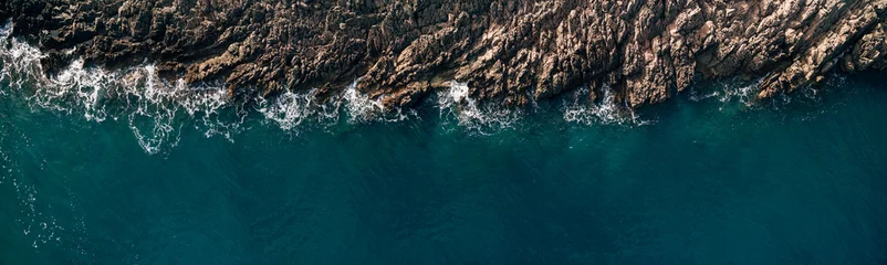 Schilderijen op glas Wild Ocean water from above - Waves hitting the rocks - aerial photography © Nadtochiy