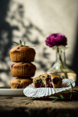 Bitten homemade cherry and chocolate muffin on wooden board with stack of three muffins on background .