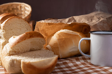Breakfast table in Brazil with breads, cheese, cup of coffee and accessories on a brown and beige checkered tablecloth, dark background, selective focus.