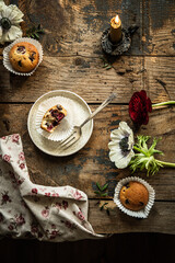 Ceramic plate with homemade cherry and chocolate muffin and vintage fork, muffins, fresh flowers and candle on old rustic wooden table.