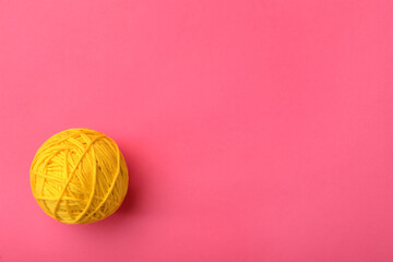 Soft yellow woolen yarn on pink background, top view. Space for text