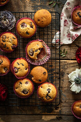 Group of homemade cherry and chocolate muffins on cooling rack and fresh flowers and leaves on rustic wooden table.