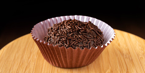 Brigadeiro, traditional Brazilian sweet in detail on wooden surface, black background, selective focus.