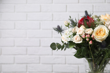 Fototapeta na wymiar Beautiful bouquet with roses against white brick wall, closeup. Space for text