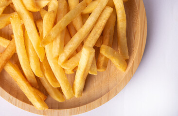 French fries placed on a round wooden plate, white background, top view.