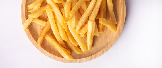 French fries placed on a round wooden plate, white background, top view.