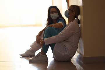 Tired women doctors are sitting in masks in corridor
