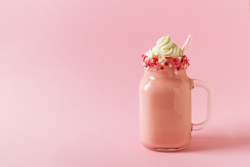 Pink milkshake with cream, marshmallow candy hearts on pink background