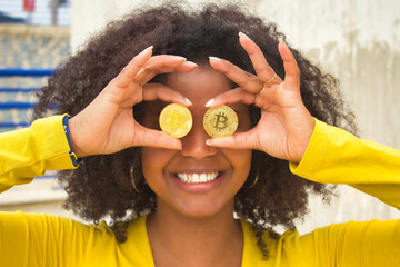 African american woman with afro hair and yellow t-shirt playing with cryptocurrencies.