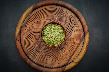 Top view of sunflower seeds in a wooden bowl on a wooden dark background.