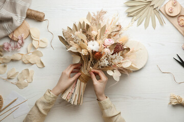 Florist making beautiful bouquet of dried flowers at white table, top view