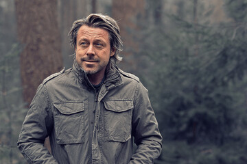 Blonde man in green coat walks in a pine forest.