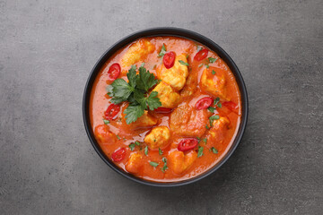 Bowl of delicious chicken curry on grey table, top view