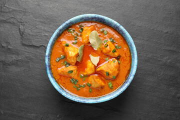 Bowl of delicious chicken curry on black table, top view