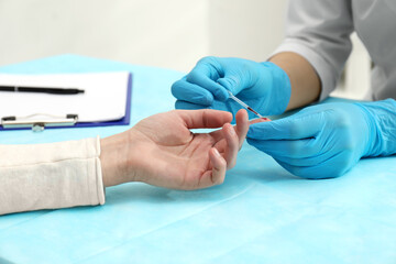 Doctor taking blood sample from patient's finger at table in clinic, closeup