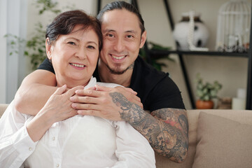 Portrait of cheerful hugging mixed-race mother and son spending weekend together at home due to pandemic