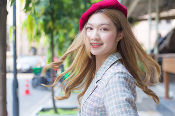 Asian beautiful lady with bronze hair wears red cap and turns to face on the street background.