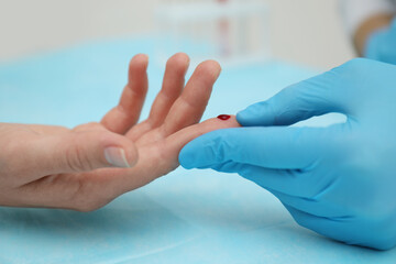 Doctor taking blood sample from patient's finger at table, closeup