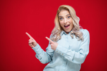 Surprised young woman while standing and pointing to blank space - copy space, promoter girl with...