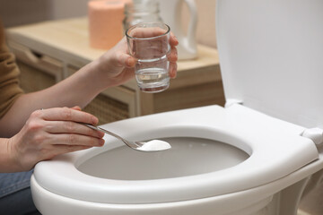 Woman cleaning toilet bowl with baking soda, indoors closeup
