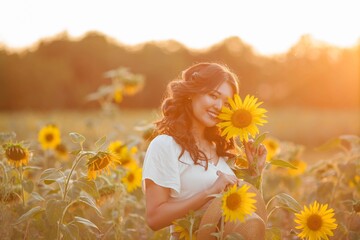 Young Asian woman with curly hair in a field of sunflowers at sunset. Portrait of a young beautiful asian woman in the sun.