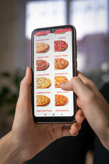 Woman holds a close-up of a mobile phone with a pizzeria website on the screen while lying on a...