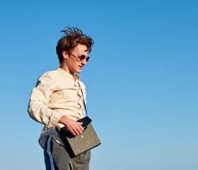 A Caucasian man from Spain standing and closing his black handbag on clear sky background