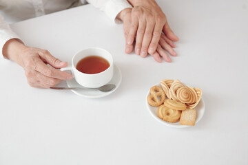 Hands of adult son touching hand of his mature woman when they are drinking tea with cookies at home